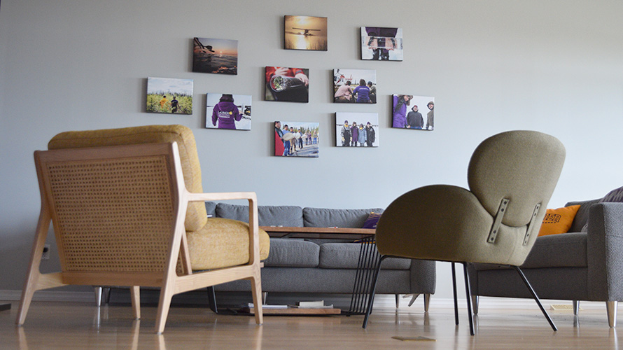 A living room with two couches, two chairs and a coffee table in front of a wall with Laurier research photos.