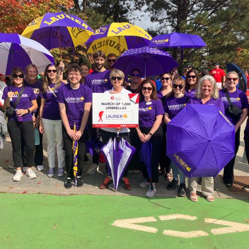 Laurier employees standing with purple and gold umbrellas.