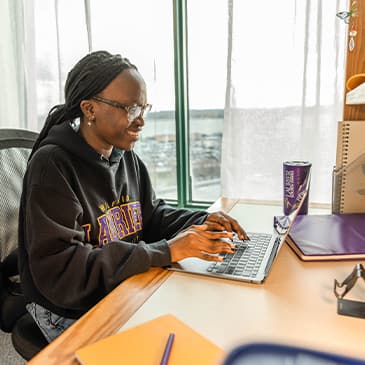 A student doing work on their laptop in a dorm room